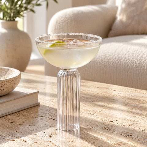 Margarita au bord salé, glaçons et quartiers de citron vert dans la coupe à champagne Torchère, canapé bouclé crème au fond