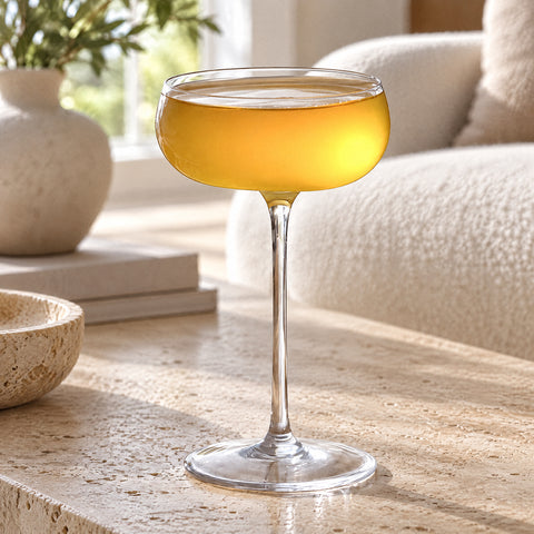 Coupe à cocktail Soprano remplie à ras bord d'un mélange orange trouble, canapé bouclette crème et vase en céramique
