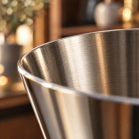 Gros plan sur le bord fin et l'intérieur d'un cône du double doseur Hakari, reflets chauds sur l'inox, étagère en bois floue en fond