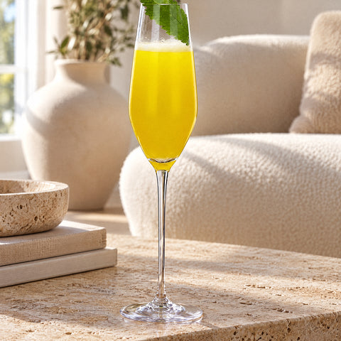 Flûte à champagne Roseau remplie de jus jaune mousseux, feuille verte sur le buvant, plateau en noyer, table en travertin
