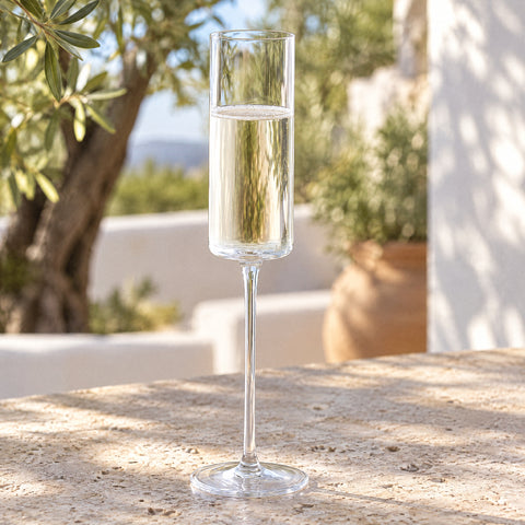 Vin effervescent pâle jusqu'à mi-calice dans la flûte à champagne Chandelle, table en pierre et oliviers flous en terrasse
