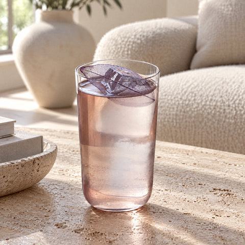 Grand verre à café Margelle rempli d'une boisson rose pâle, feuille violette sur le bord, canapé bouclette crème