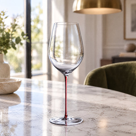 Grand verre à vin rouge Vocalise vide, tige à filet rouge, sur une table en marbre, fauteuil en velours vert et suspension dorée flous