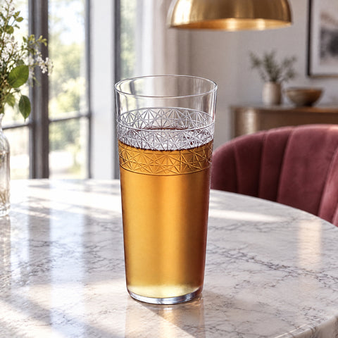 Verre highball Croisillon garni d'une boisson ambrée, sur une table ronde en marbre blanc sous une suspension en laiton