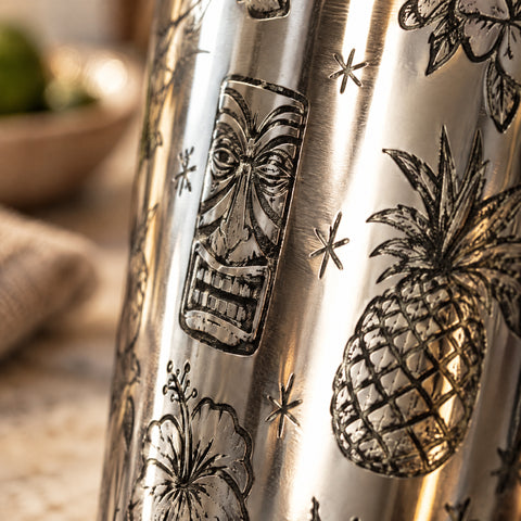 Gros plan sur la paroi gravée du shaker Palmeraie : mug tiki et ananas en traits fins, inox miroir et long reflet blanc