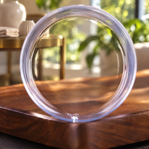 Tumbler à filets gravés Frise vu de face, cercle transparent sur une planche en bois, desserte en laiton et plantes floues