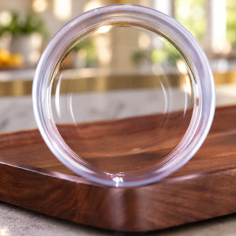 Gros plan sur le fond épais et circulaire du verre à cocktail Ondée, anneaux de lumière concentriques, plateau en noyer