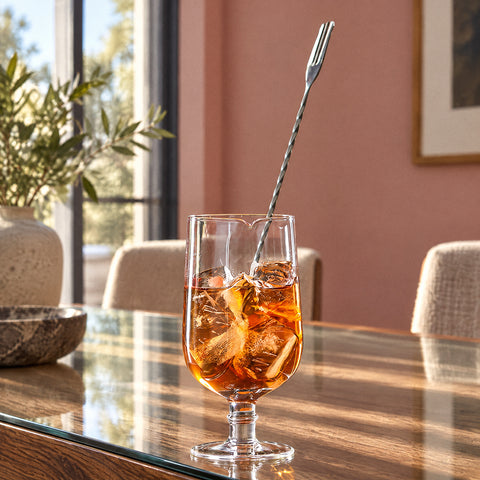 Verre à mélange à pied Balustre au cocktail ambré glacé, cuillère torsadée en biais, mur rose poudré et hautes fenêtres