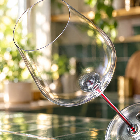 Gros plan sur le calice incliné du verre à vin Pigment, filet rouge naissant dans la tige, carrelage vert flou au fond