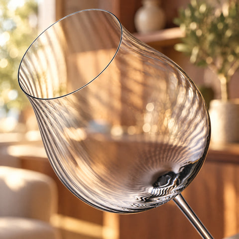 Gros plan sur le calice du verre à vin tulipe Hélice, côtes en spirale descendant du buvant, meuble bar en noyer flou