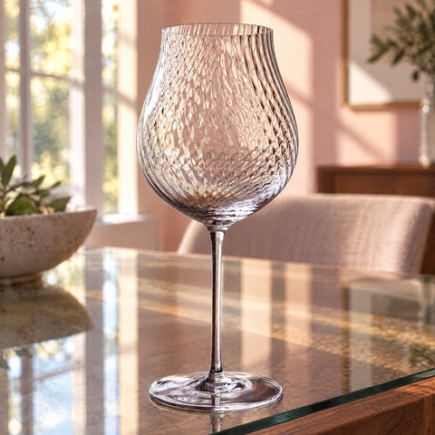 Le verre à vin tulipe Hélice vide, debout devant un mur rose poudré et de hautes fenêtres floues
