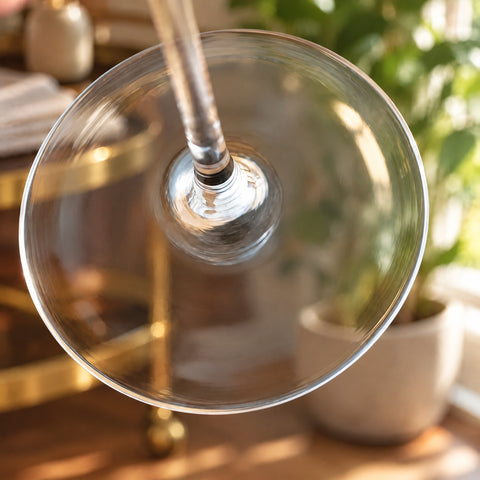 Gros plan sur le pied rond et la base de la tige du verre ballon digestif Alcôve, desserte en laiton et plante floues