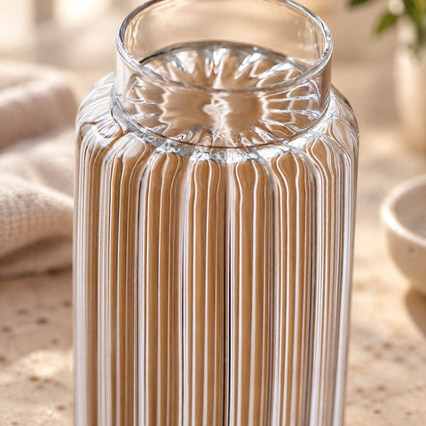Gros plan sur le buvant lisse et les cannelures verticales du verre long drink Prêle, linge beige et bol en céramique flous en arrière-plan.