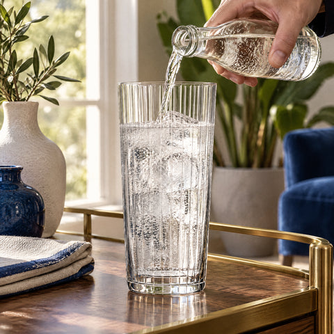 Main versant du tonic sur glaçons et gin dans le verre long drink Orgue, desserte en laiton et noyer, vases en céramique