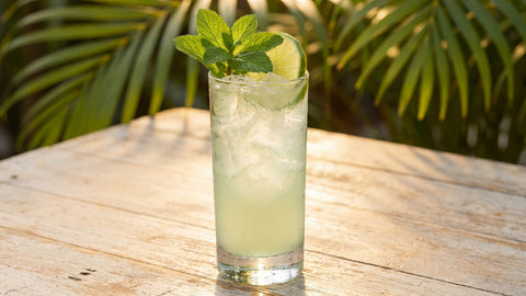 Mojito cubain au rhum blanc dans un verre highball avec glace pilée, menthe et citron vert sur table en terrasse