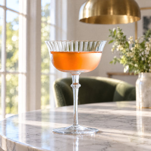 Coupe à cocktail côtelée Éventail embuée, remplie d'une boisson ambrée, suspension en laiton et fauteuil en velours flous