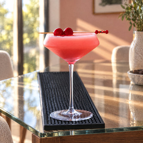 Coupe à cocktail japonaise Apex remplie d'un cocktail rouge rosé, pique à deux cerises sur le bord, mur rose poudré