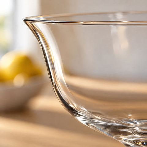 Gros plan sur le bord évasé et la courbe du calice de la coupe Lotus, citron et bol flous derrière, comptoir clair