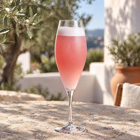 Cocktail pétillant rose pâle et mousse blanche dans la flûte à champagne Lys, terrasse méditerranéenne et oliviers