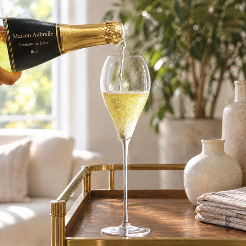 Main versant un vin effervescent doré d'une bouteille étiquetée dans la flûte à champagne Navette, sur une table en bois