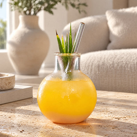 Verre à cocktail Siphon rempli d'une boisson jaune glacée avec paille en verre et feuille d'agave, canapé bouclette crème