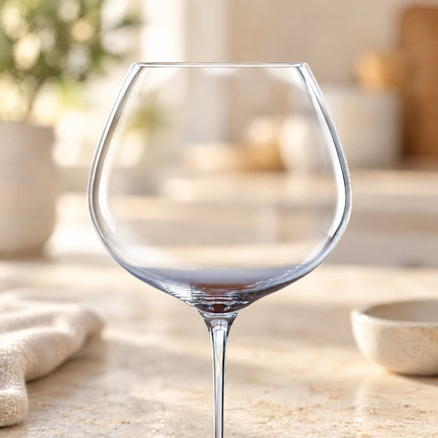 Gros plan sur le calice rond du grand verre ballon Baryton, légère trace de vin rouge, travertin et torchon en lin flous