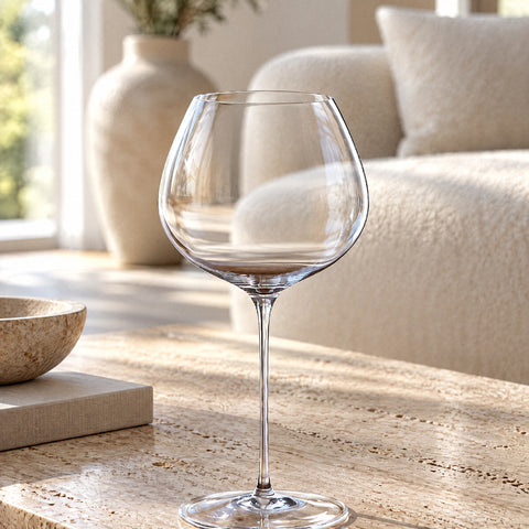 Le grand verre ballon Baryton seul sur une table, reflets sur la tige, canapé en bouclette crème et vase en céramique flous