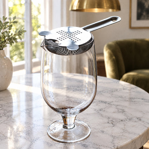 Passoire à ressort en inox posée sur le mixing glass à martini Lanterne, suspension en laiton et fauteuil en velours