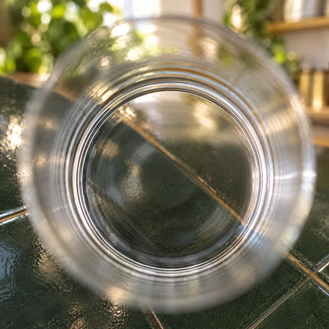 Gros plan sur le verre à whisky Versant vu d'en haut, anneaux concentriques dans le verre, carrelage vert et plantes flous autour