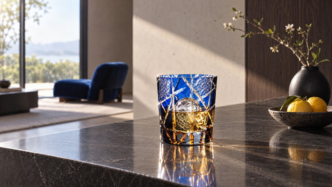 Verre à whisky Edo Kiriko Verasco en cristal taillé bleu et ambre sur un comptoir en basalte, intérieur japonais moderne, fauteuil bleu