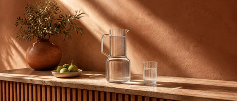 Carafe d'eau | Carafe d'eau en verre Verasco avec verre à eau assorti sur un plan de travail en travertin, branche d'olivier et figues fraîches