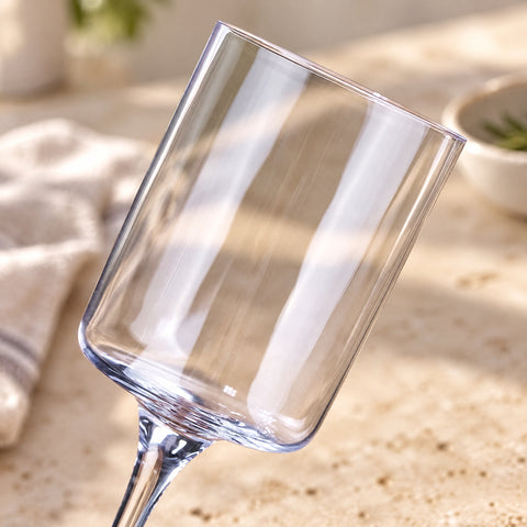 Gros plan incliné sur le buvant cylindrique et la jambe fine du verre à cocktail Semplice, serviette et bol flous sur une pierre beige