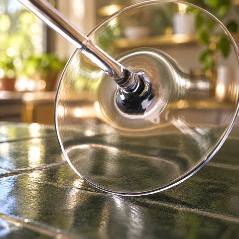Gros plan sur le pied fin et la base de la tige du verre à grappa Globe sur une table en bois, fond flou de carrelage vert