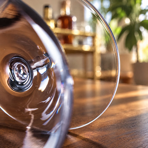 Gros plan sur le verre à martini Largo couché sur une table en bois, flacon ambré et étagère en laiton flous à l'arrière.