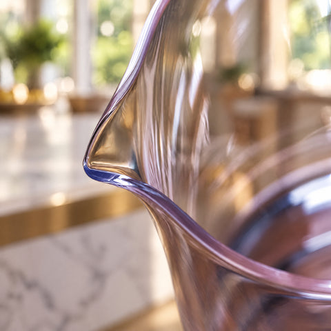 Gros plan sur le bec verseur pincé du verre à mélange lisse Remous, comptoir en marbre à liseré laiton et fenêtres lumineuses floues.