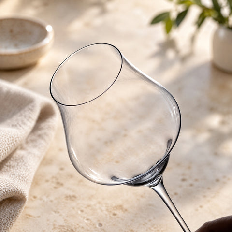 Gros plan sur le buvant fin et le calice tulipe du verre à vin Mât, devant un comptoir en travertin flou