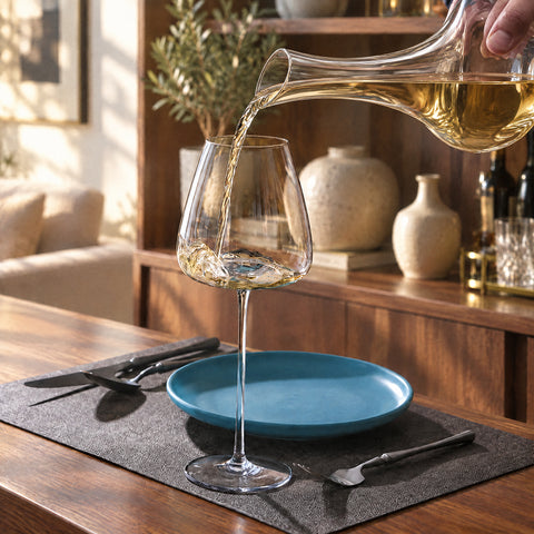 Vin blanc doré versé d'une carafe en cristal dans le verre à vin Soprano, assiette bleu canard et set de table gris foncé