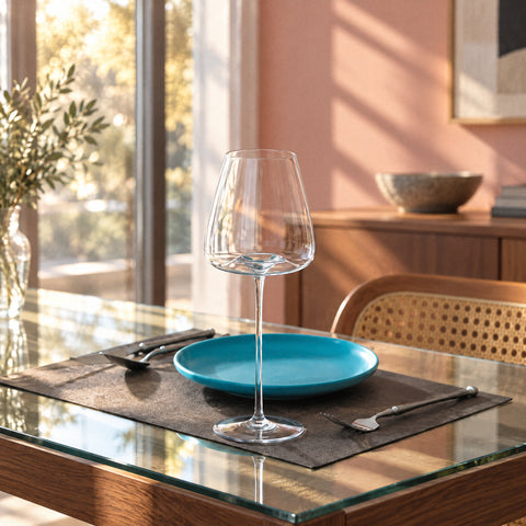 Le verre à vin Soprano dressé sur une table avec assiette bleu canard et couverts, mur rose poudré et hautes fenêtres