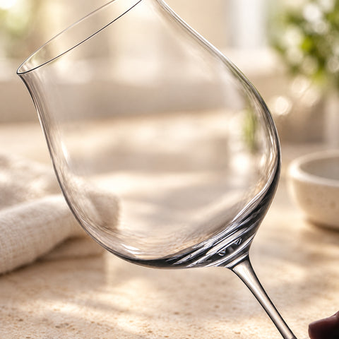 Gros plan sur le calice du verre à vin pied bas Tablée, buvant fin, plan de travail en travertin et torchon de lin flous