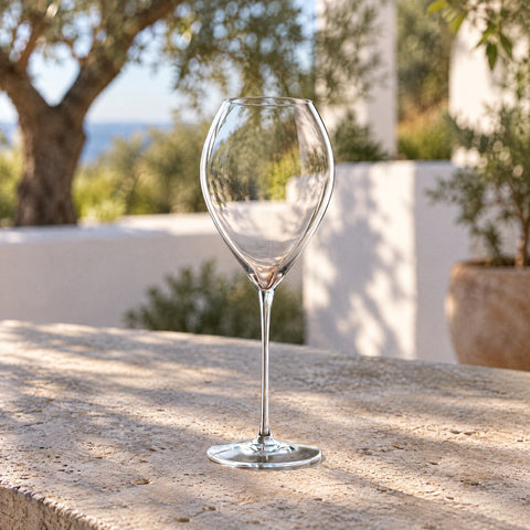 Le verre à vin de dégustation Étrave sur une table de terrasse méditerranéenne, oliviers et murs blancs flous