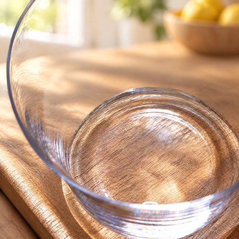 Gros plan sur la base ronde et la paroi évasée du verre à whisky évasé Estuaire, plan de travail en bois et citrons flous