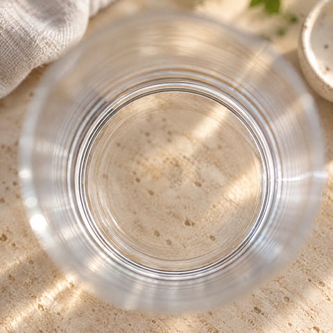 Gros plan sur le verre à whisky Plume vu d'en haut, anneaux concentriques dans le verre, pierre claire, linge et coupelle flous