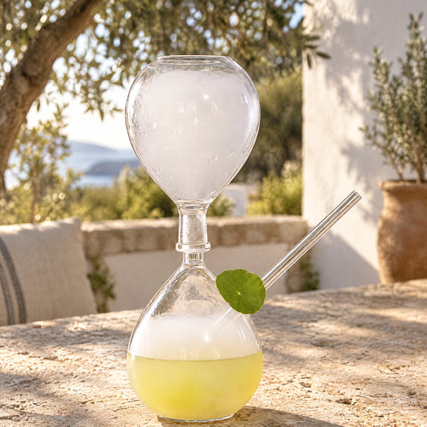 Verre avec paille intégrée Fumerolle, fumée blanche en haut et cocktail jaune pâle en bas, table en pierre et oliviers