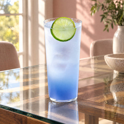 Cocktail dégradé bleu et blanc dans le verre café glacé Carène, rondelle de citron vert au bord, table vitrée et mur rose