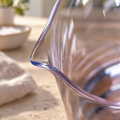 Gros plan sur le bec verseur pincé du verre de mixologie Remous, plan en pierre claire, bol blanc et linge beige flous à l'arrière.