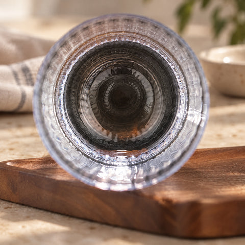 Gros plan sur le fond épais du verre long drink cannelé Arpeggio vu par-dessous, anneau de lumière, planche en bois sombre