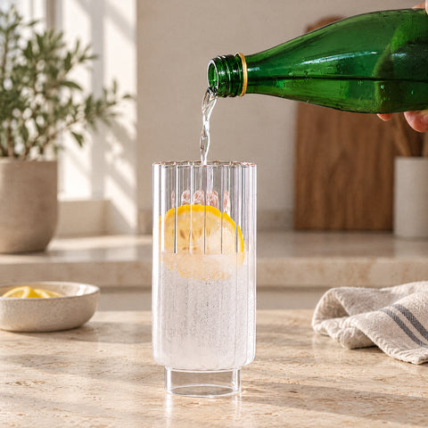 Main versant de l'eau pétillante d'une bouteille verte dans le verre long drink Prêle, rondelle de citron, torchon en lin