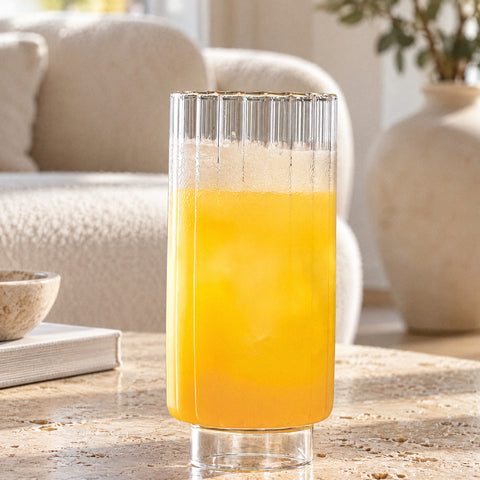 Jus d'orange et glaçons dans le verre long drink Prêle, canapé bouclette crème et vase en céramique en fond